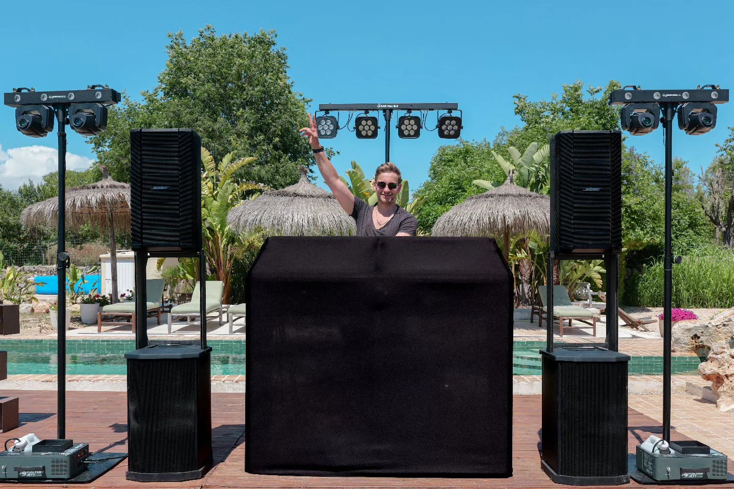 DJ Robinho hinter seinem DJ-Pult mit Lautsprechern und Lichttechnik an einem Pool