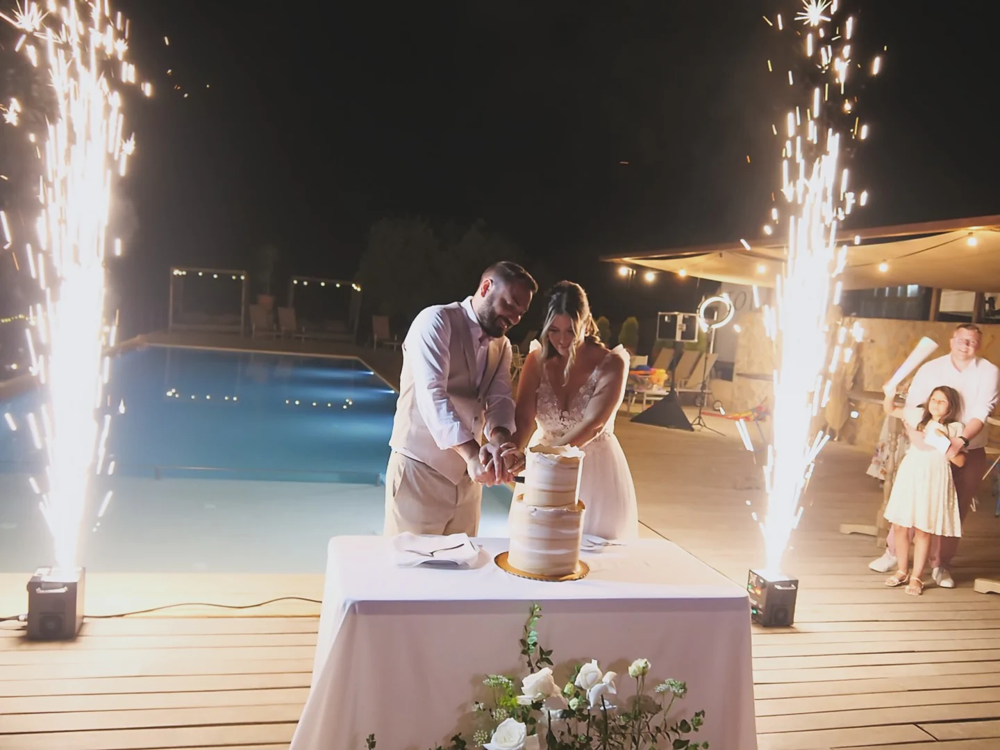 Brautpaar schneidet die Hochzeitstorte am Pool einer Finca auf Mallorca, umrahmt von Cold Sparkling Fountains